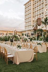 Luxury garden wedding setup with white and gold furniture, lush floral arrangements, and tropical palm tree backdrop.