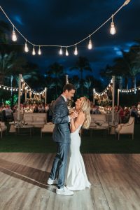 Luxury garden wedding setup with white and gold furniture, lush floral arrangements, and tropical palm tree backdrop.